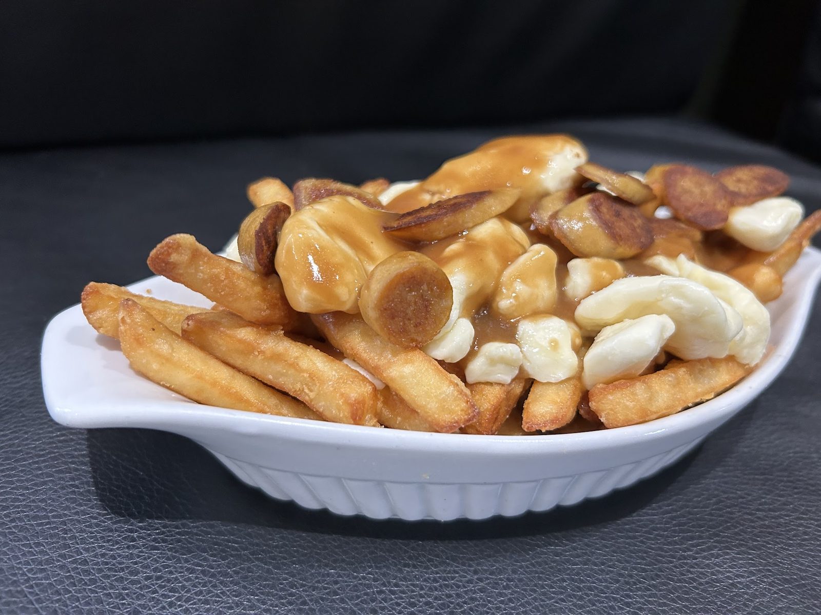 Une poutine servie dans un plat ovale blanc : frites, fromage en grains et sauce.