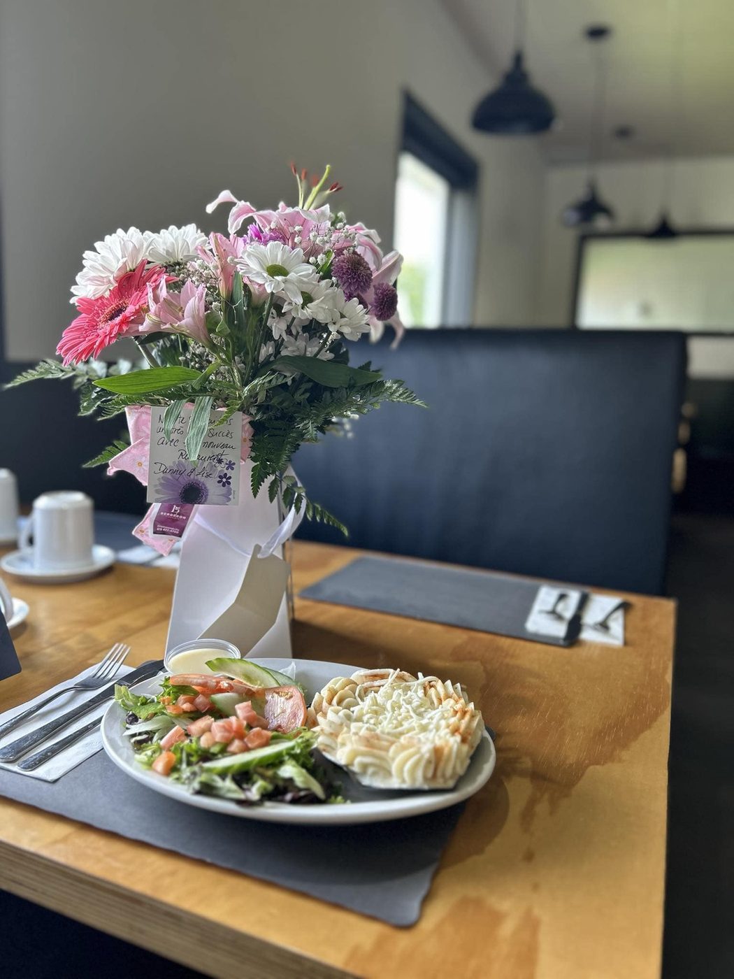 Une table de la salle à manger : plateau de bois, napperon d'ardoise, banquette marine, et une assiette de pâté chinois avec salade.